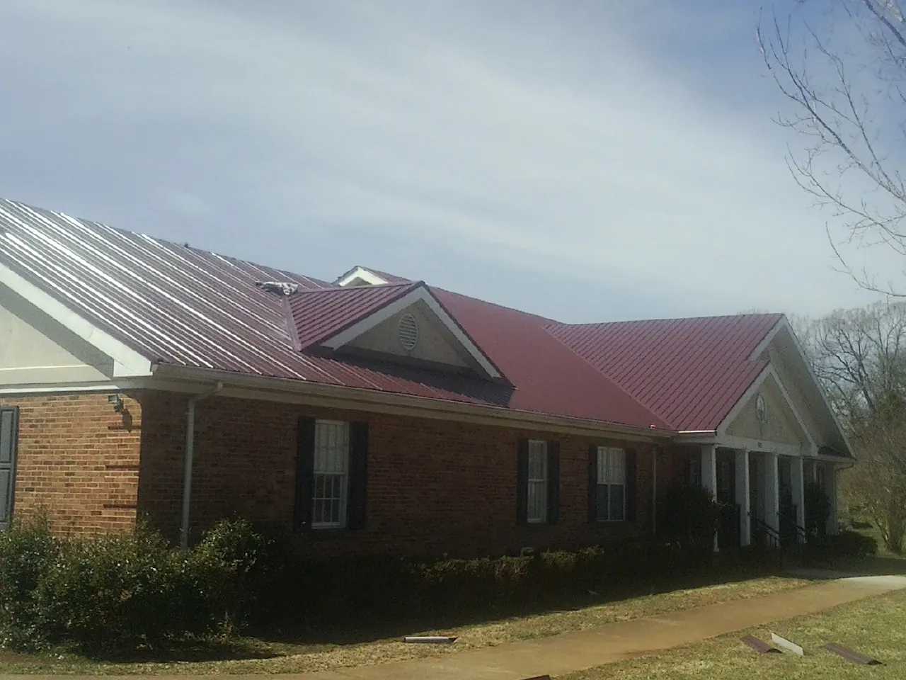 Red metal roof with gabled entries on a long brick building, from a Hail Damage Roof Repair job in Stafford Springs