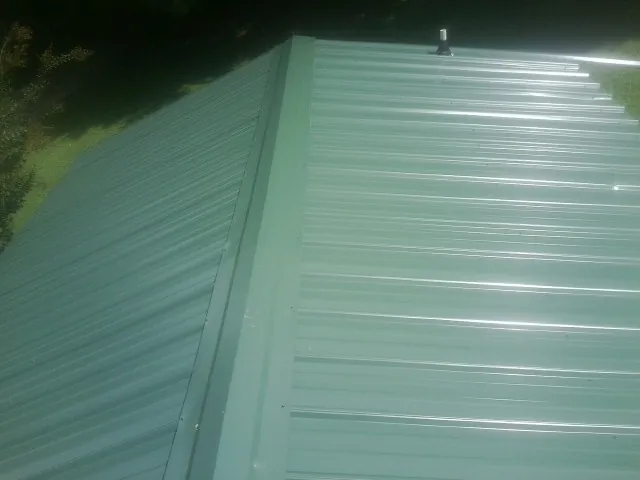 New green metal panels meeting at the ridge of a roof — Flat Roof Repair work by our crew in Stafford Springs