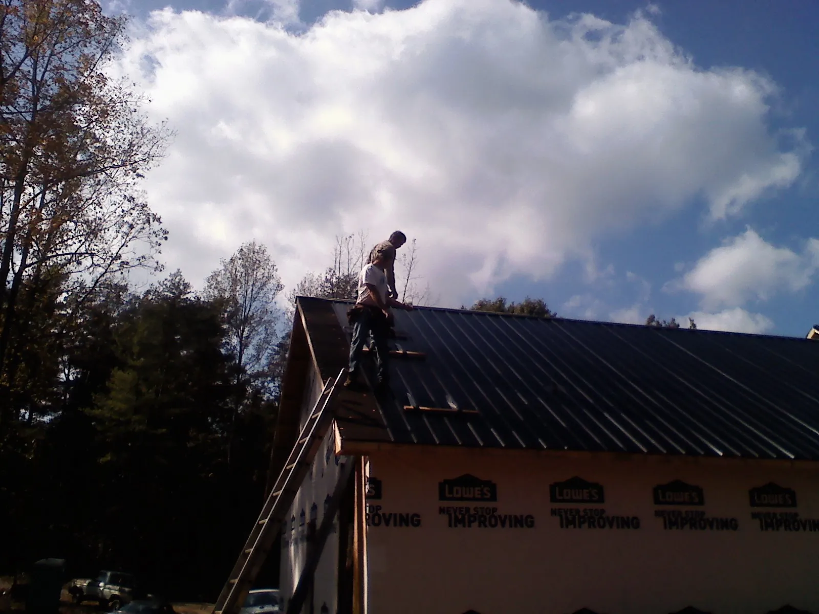 Roofer fastening dark metal panels high against a cloudy sky, from a Roof Inspection job in Stafford Springs