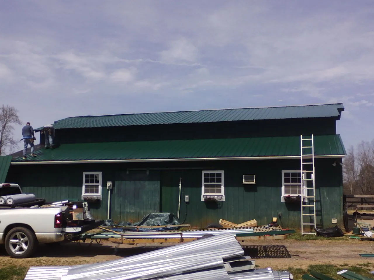 Crew installing green metal roofing on a large green barn in Stafford Springs