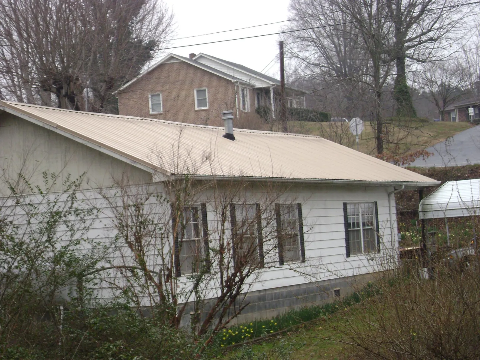 Tan metal roof on a white sided house set into a hillside — Commercial Roofing by Roofing Brothers in Stafford Springs